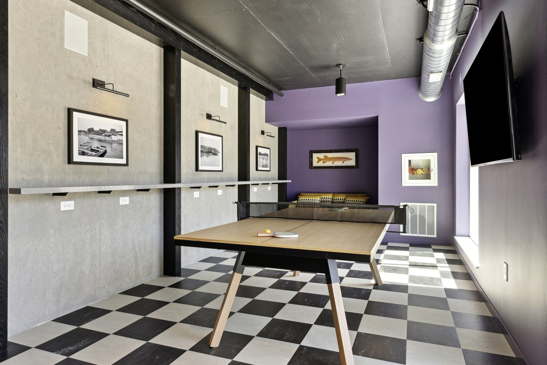 Indoor community game room with a ping-pong table, checkered floor, purple walls, and a wall-mounted TV at Esox House in St. Paul, MN.