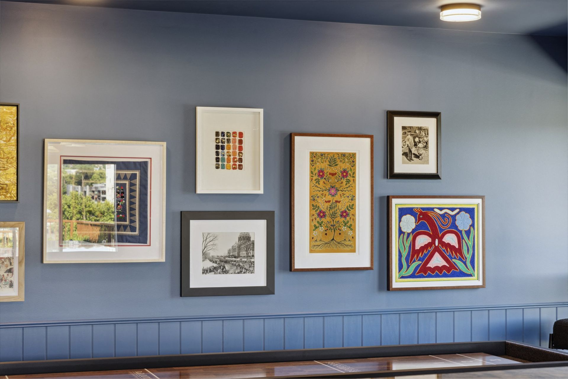 Blue wall with a gallery of framed artworks arranged in a hallway/lobby at Esox House in St. Paul, MN.