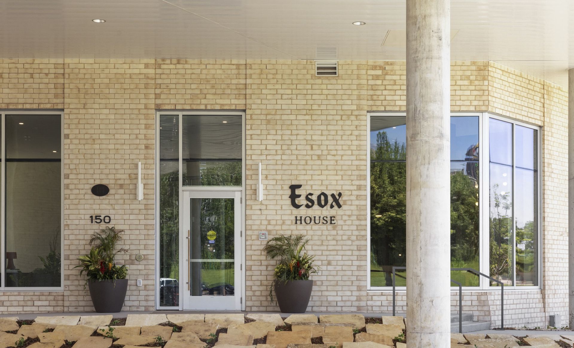 Exterior building entrance with brick facade, glass door, and potted plants at Esox House in St. Paul, MN.