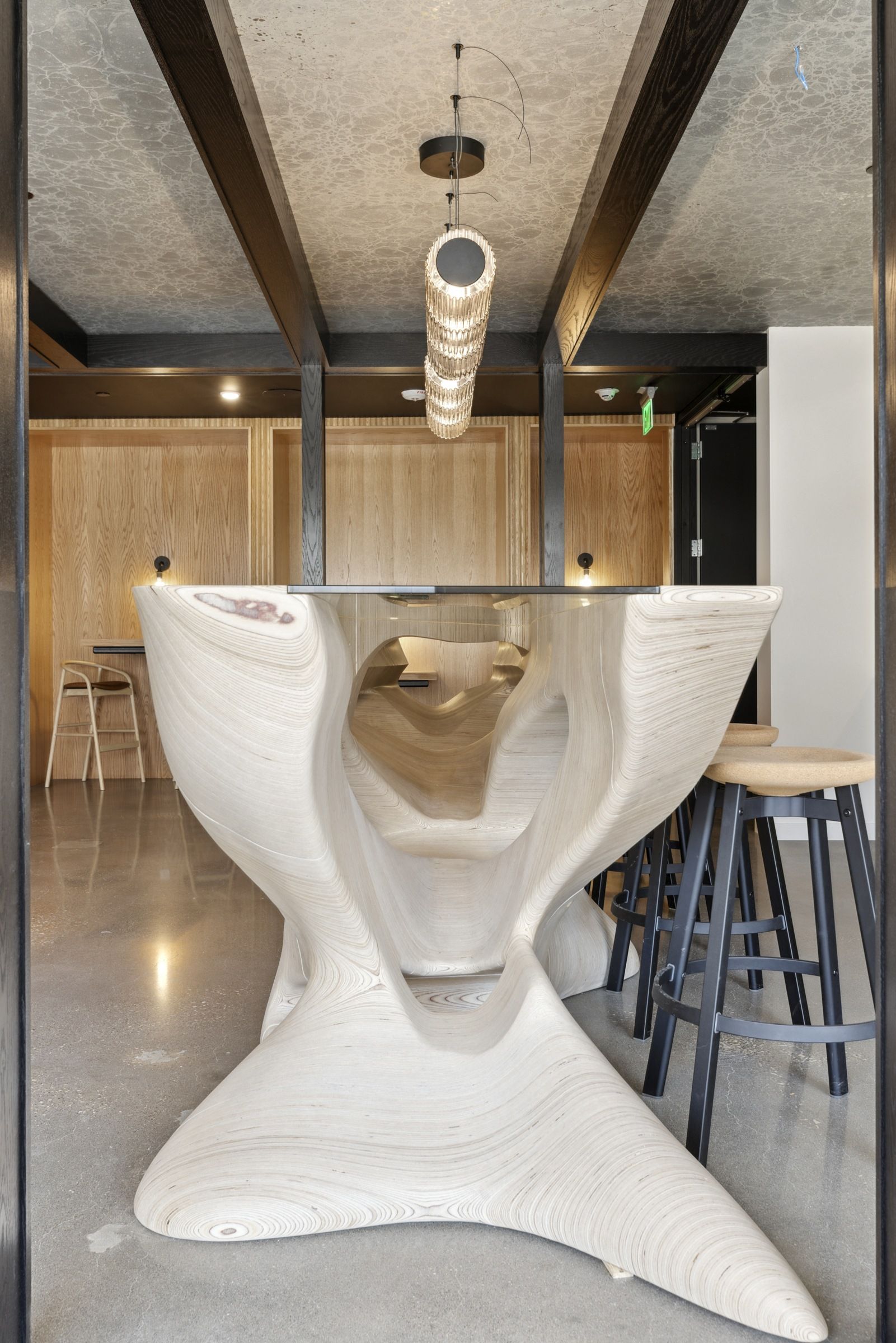 Interior lobby with a sculptural wooden table, pendant light, and bar stools at Esox House in St. Paul, MN.