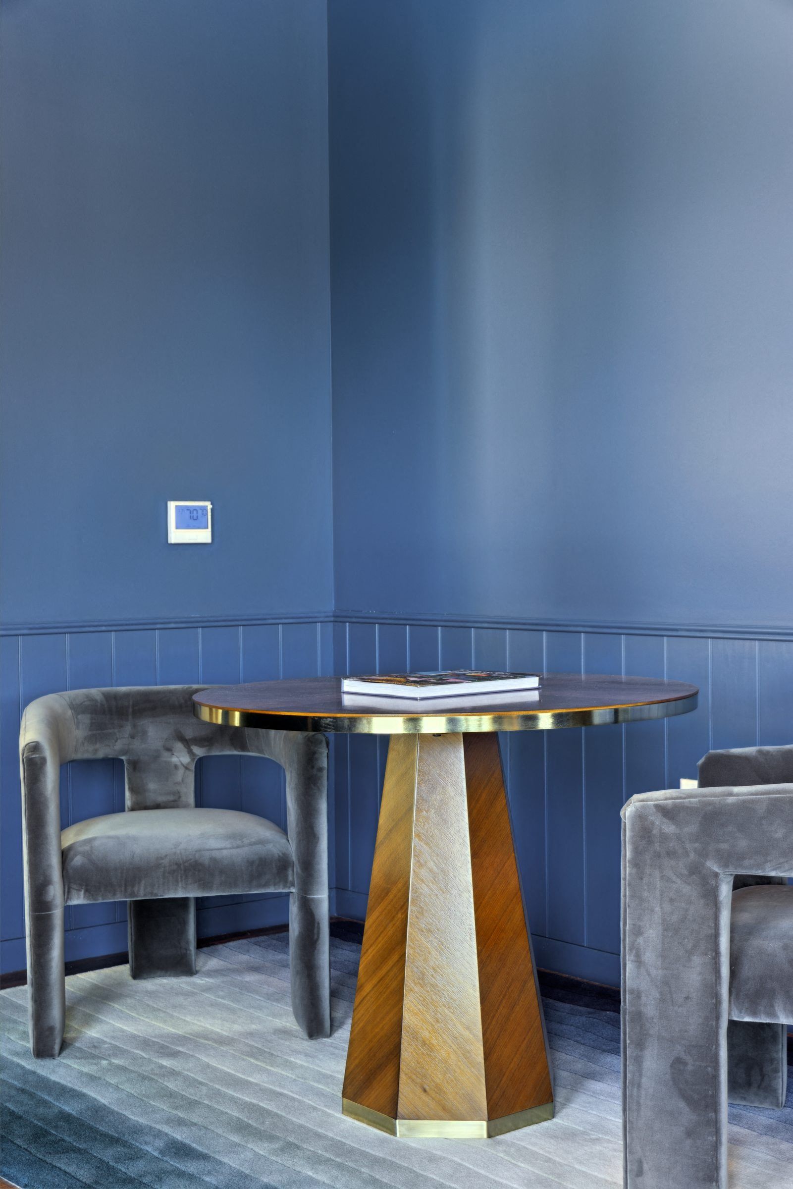 Blue-walled lounge with a round wooden pedestal table and gray upholstered chairs at Esox House in St. Paul, MN.