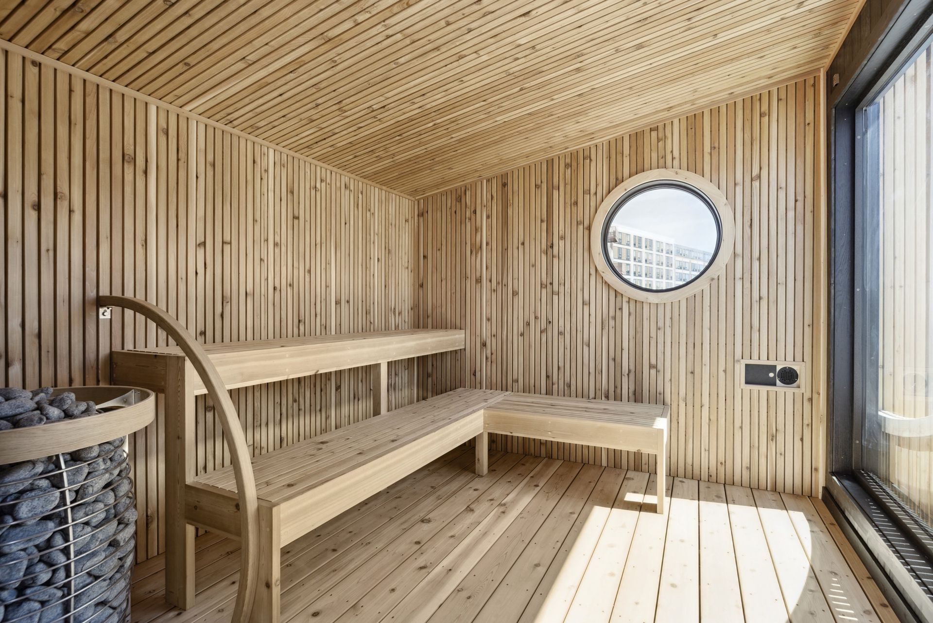 Wood-paneled sauna interior with round window and two-tier benches at Esox House in St. Paul, MN.