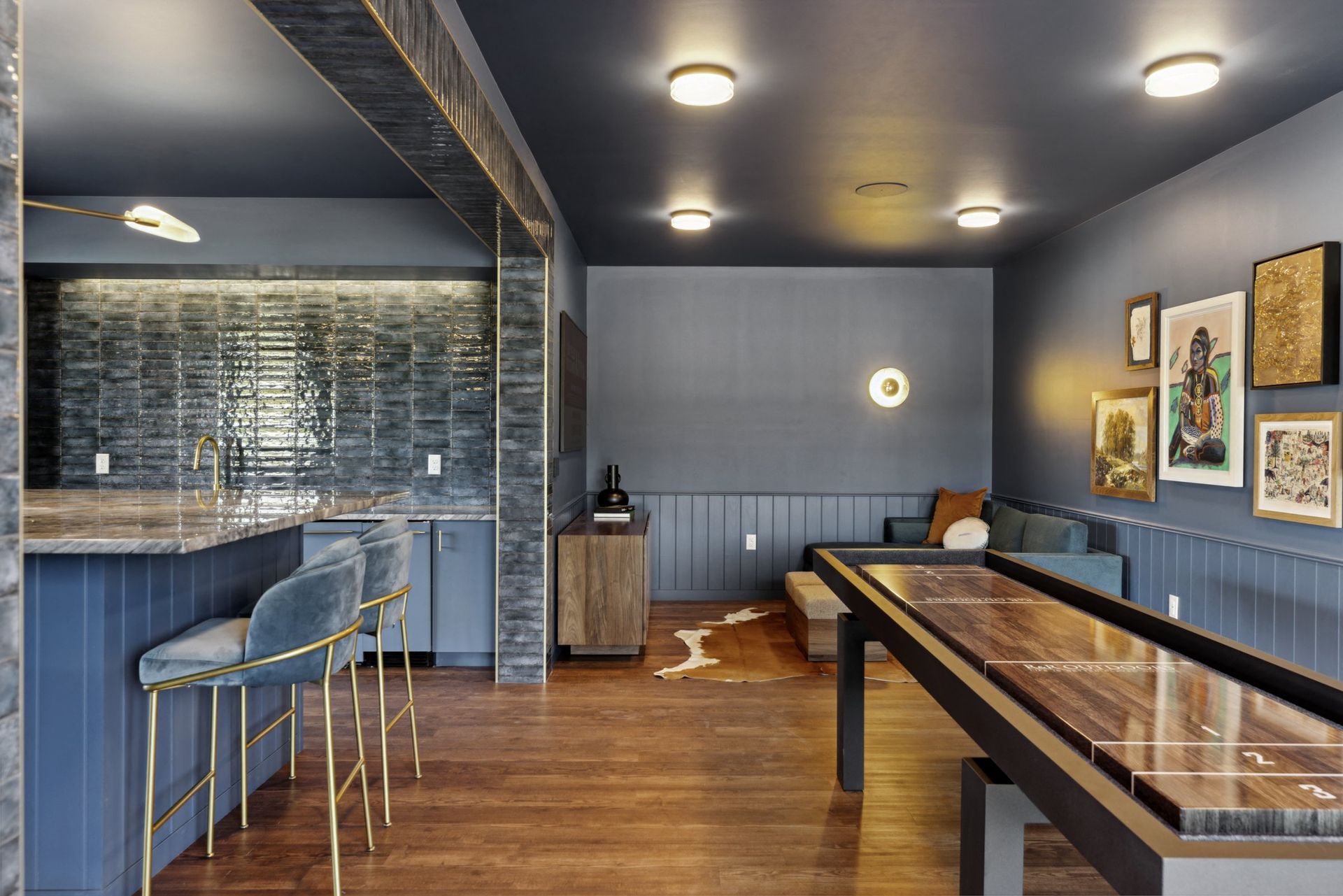 Interior community lounge with blue walls, bar seating, a long walnut game table, and wall art at Esox House in St. Paul, MN.