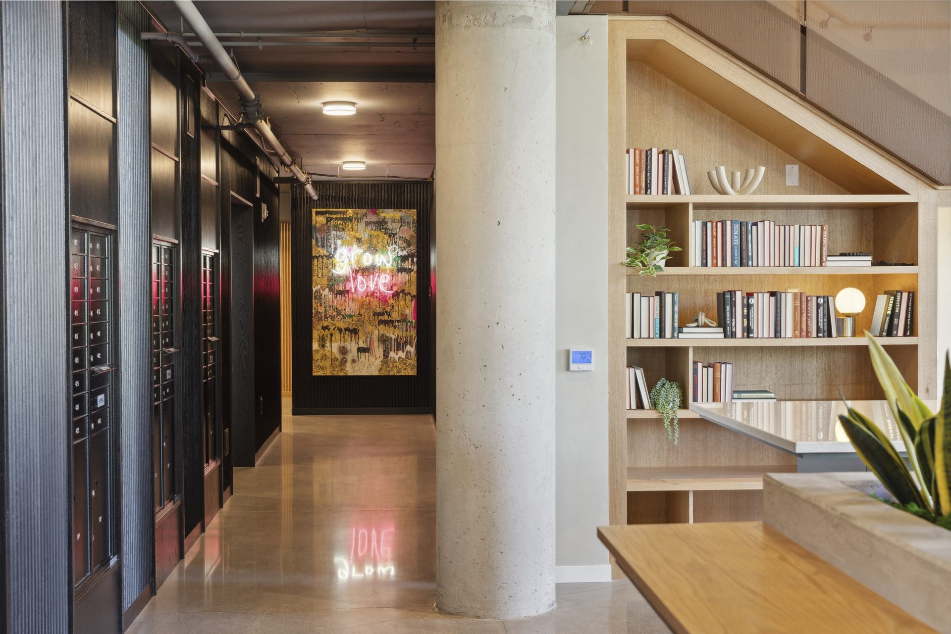 Interior hallway with a concrete pillar, dark lockers on the left, and a wooden bookshelf on the right at Esox House in St. Paul, MN.