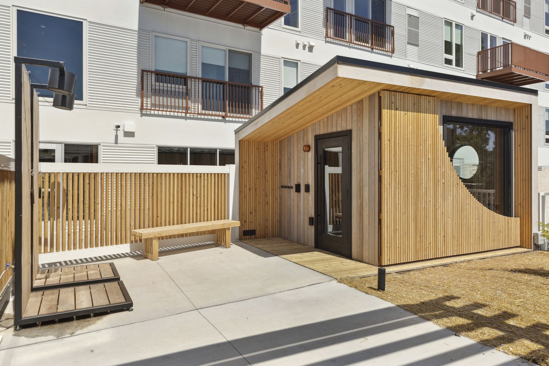Wood-clad community amenity building with a glass entry door, curved window cutout, and surrounding wooden fence at Esox House in St. Paul, MN.