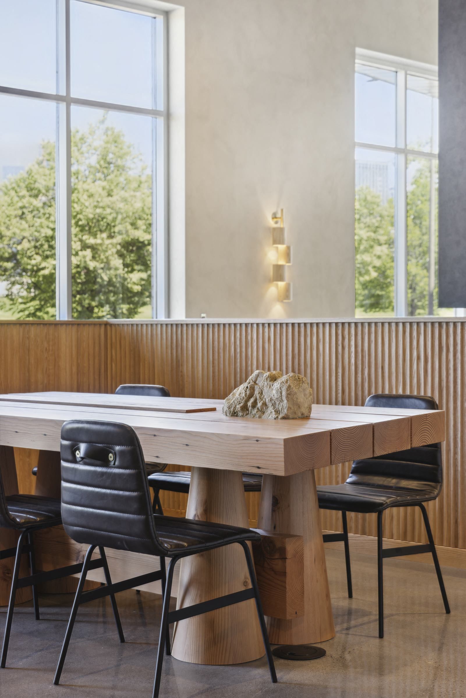 Interior view of a bright communal dining area with a large wooden table, black chairs, and tall windows at Esox House in St. Paul, MN.