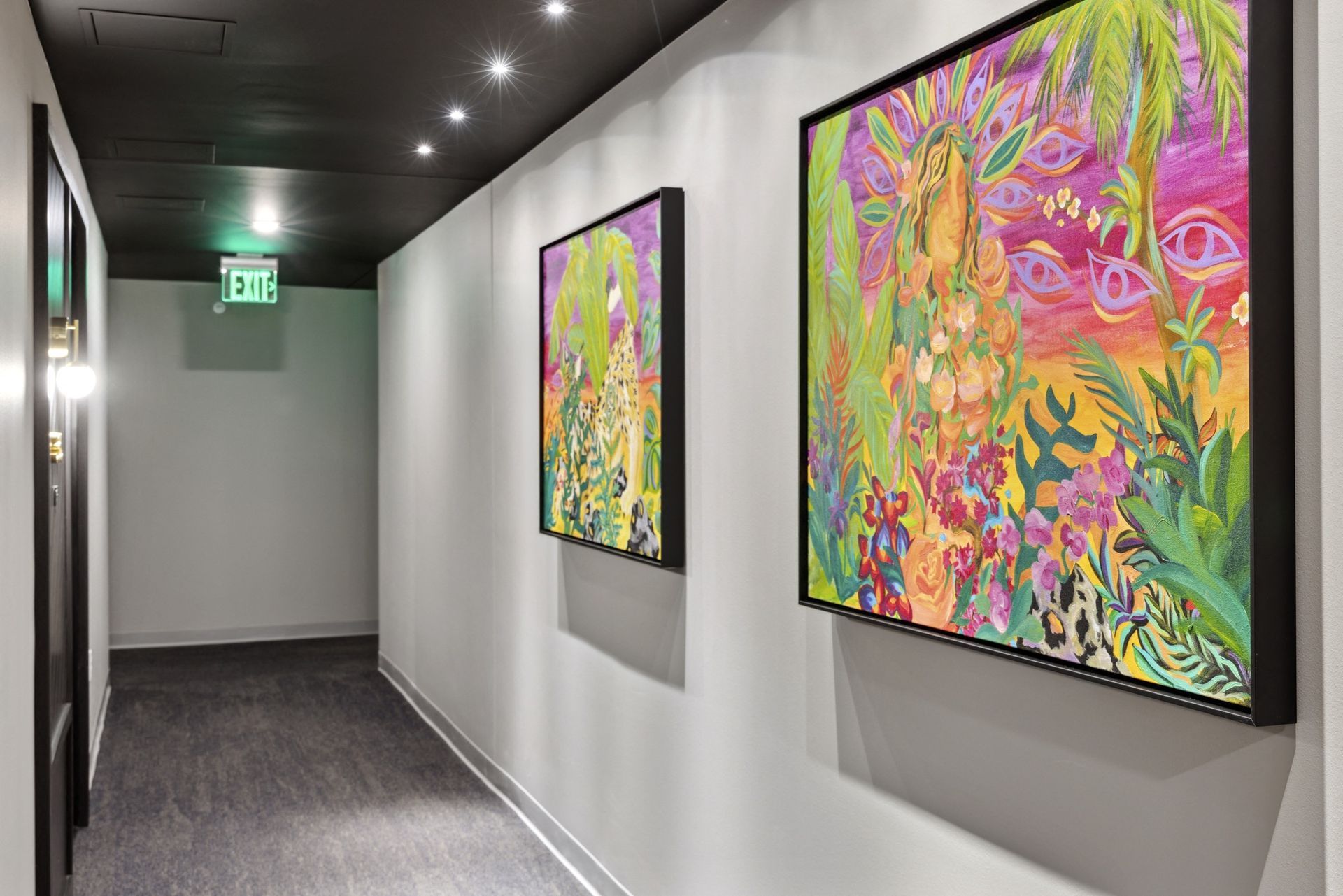 Hallway in a residential building with white walls, dark ceiling, and two large colorful framed paintings at Esox House in St. Paul, MN.