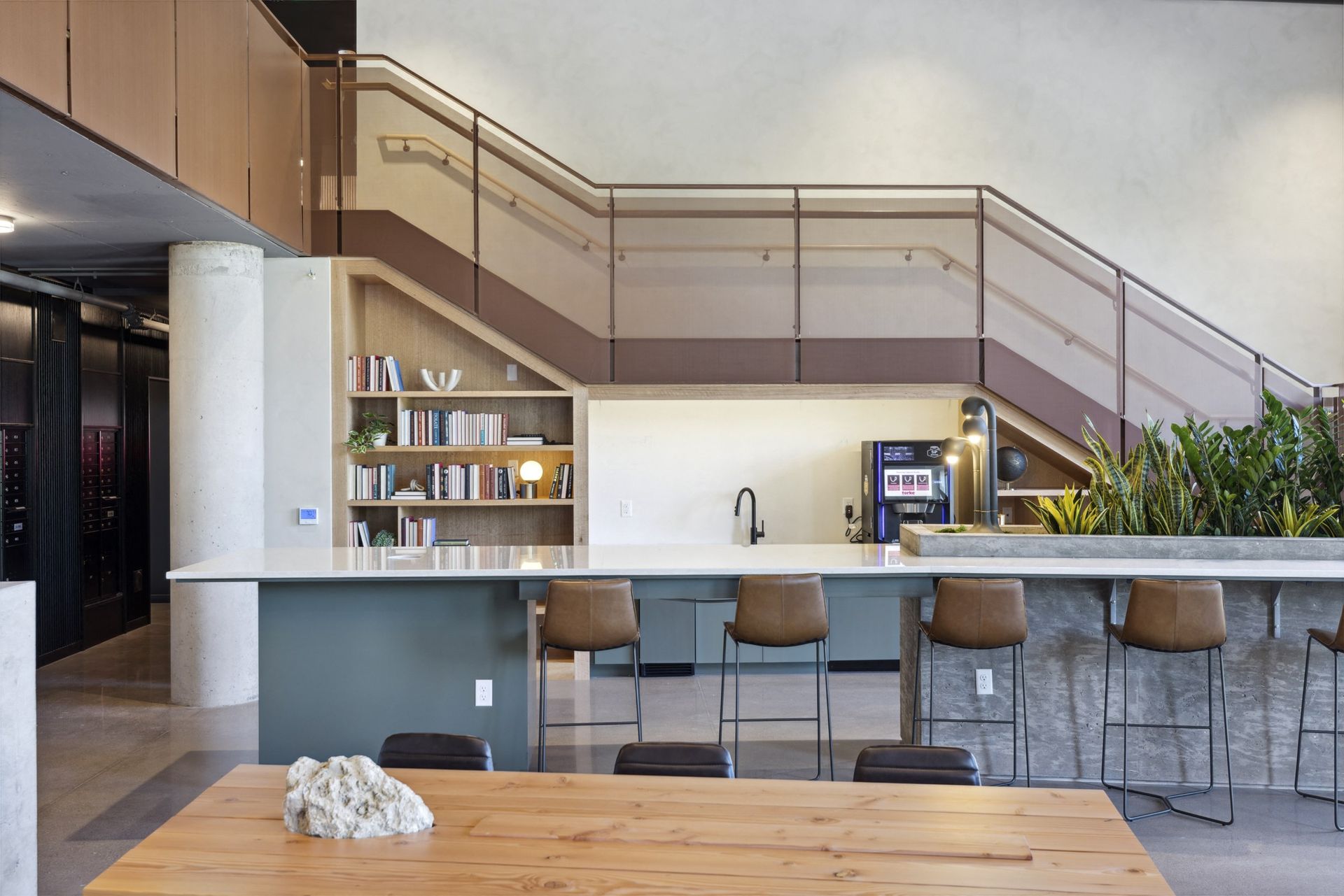 Open-concept community space with a long counter, bar stools, bookshelves, and a staircase at Esox House in St. Paul, MN.