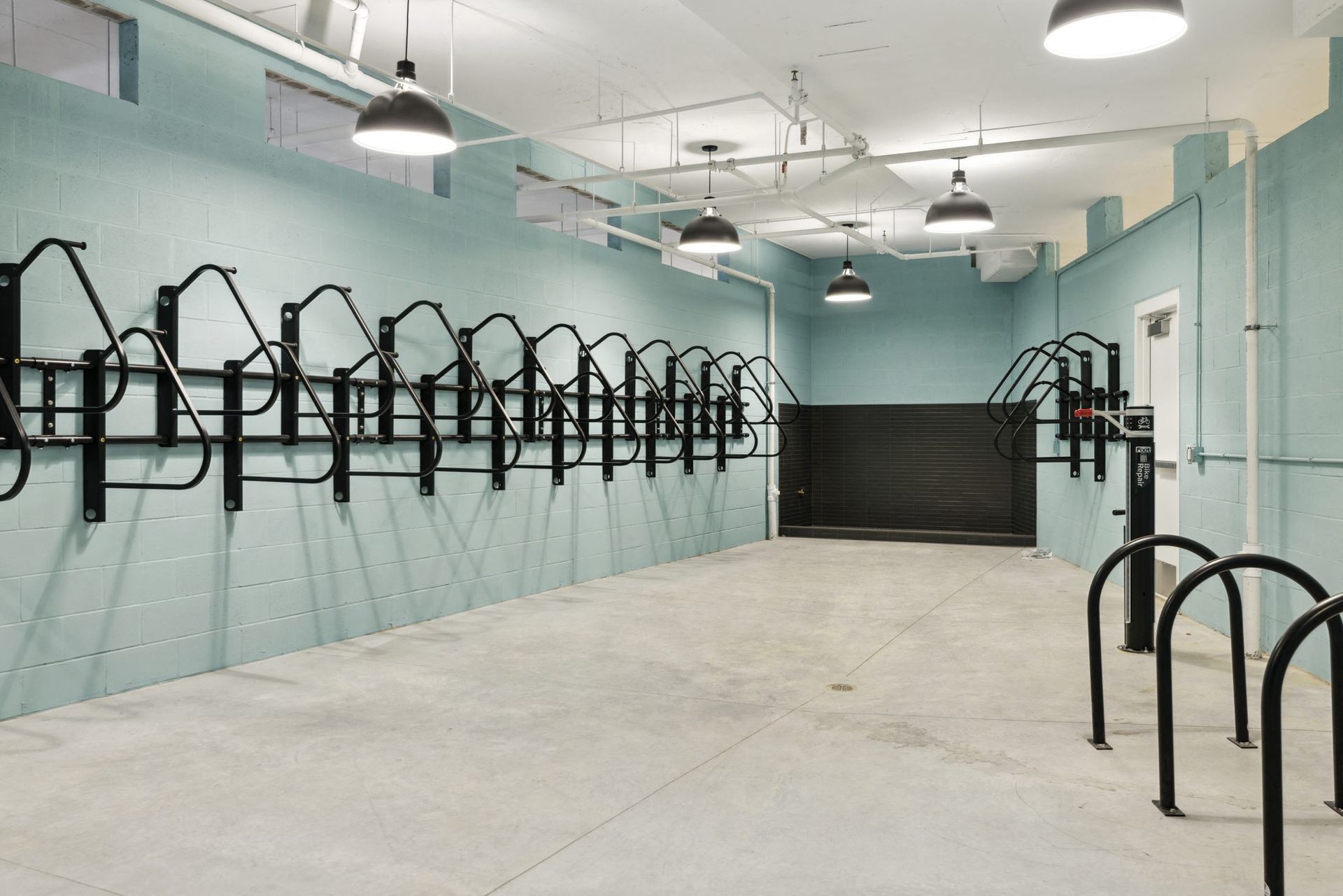 Indoor bike storage area with turquoise walls and a long row of black metal racks at Esox House in St. Paul, MN.