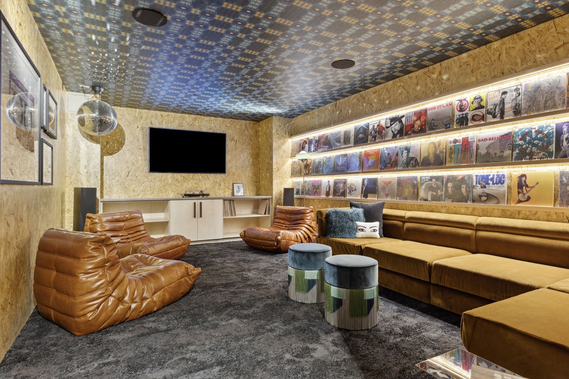 Retro-inspired resident lounge with a vinyl-record wall, tan leather seating, and a central media area at Esox House in St. Paul, MN.