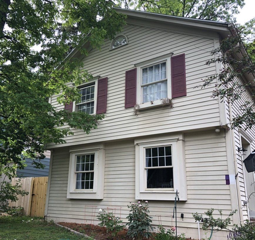 Painter using a ladder to reach and paint the upper level of a residential home.