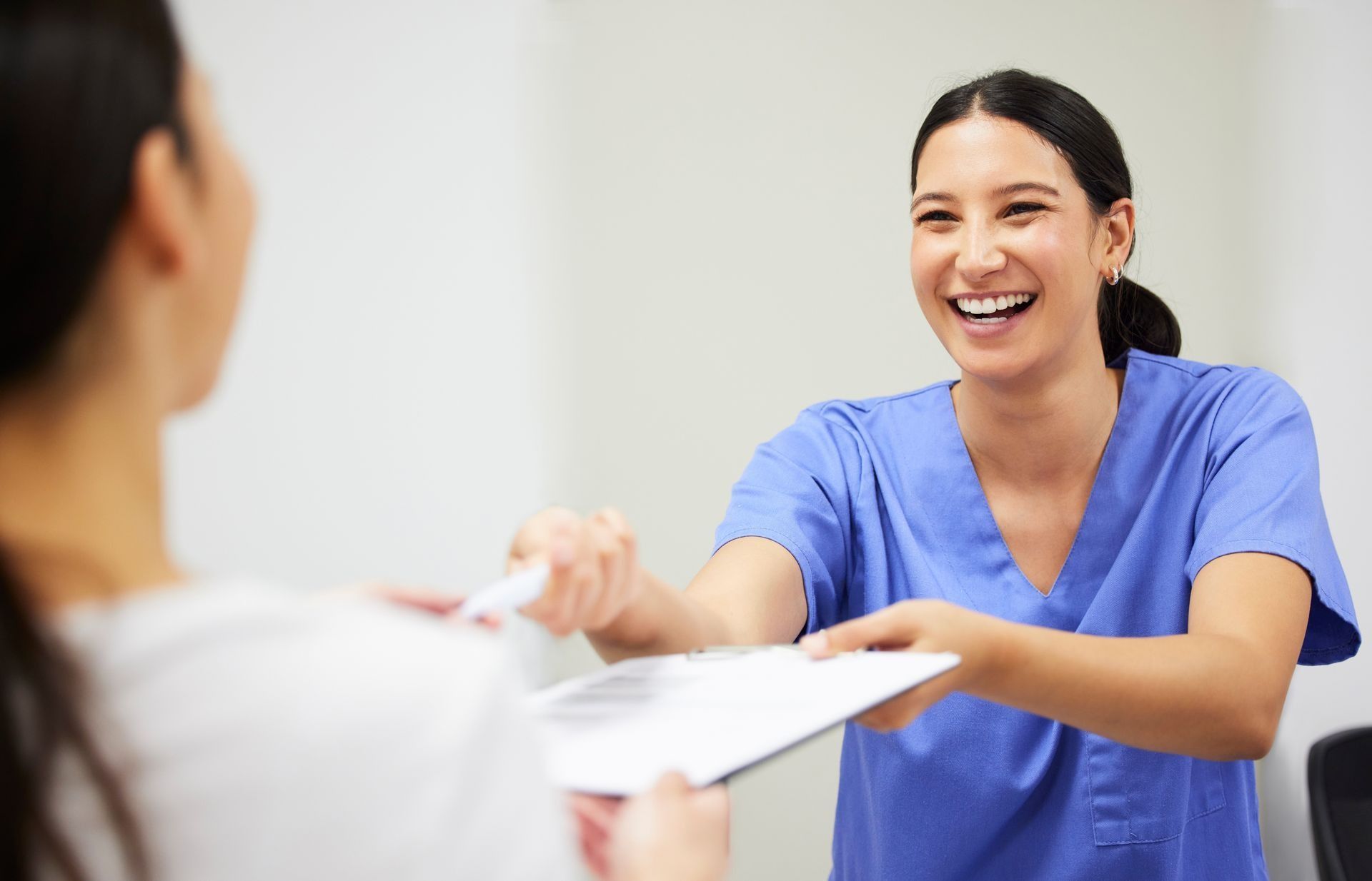 Nurse in blue scrubs smiling while handing paperwork to a patient.
