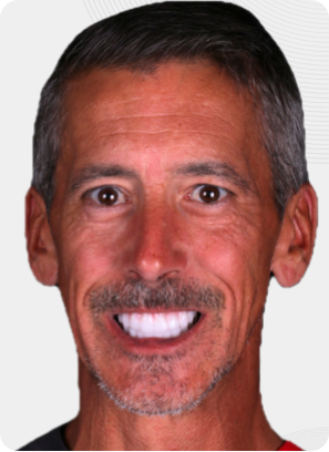 Man smiling, showing white teeth, with graying hair and mustache.