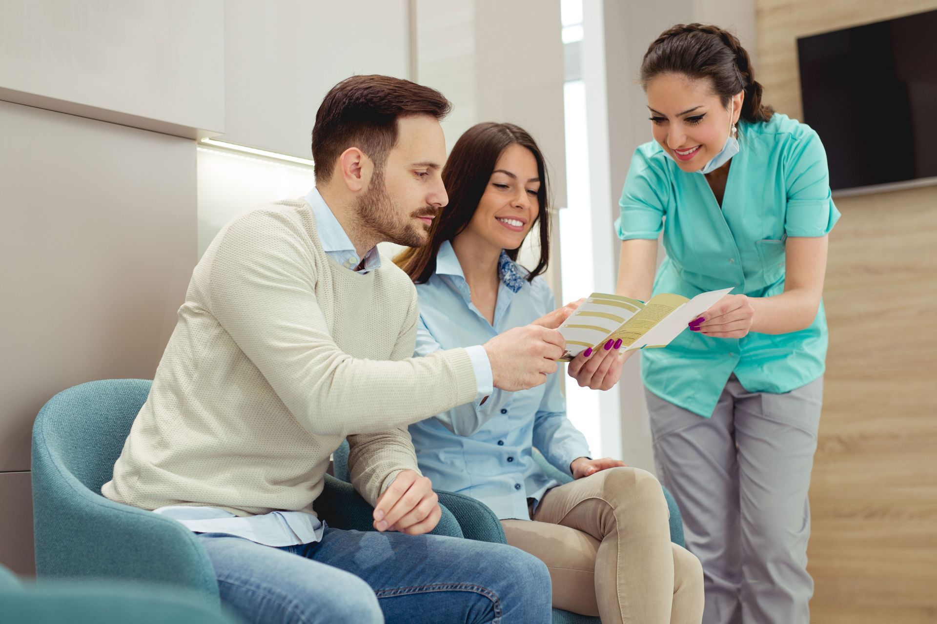 Couple in a dental office looking at a brochure with a dental assistant.