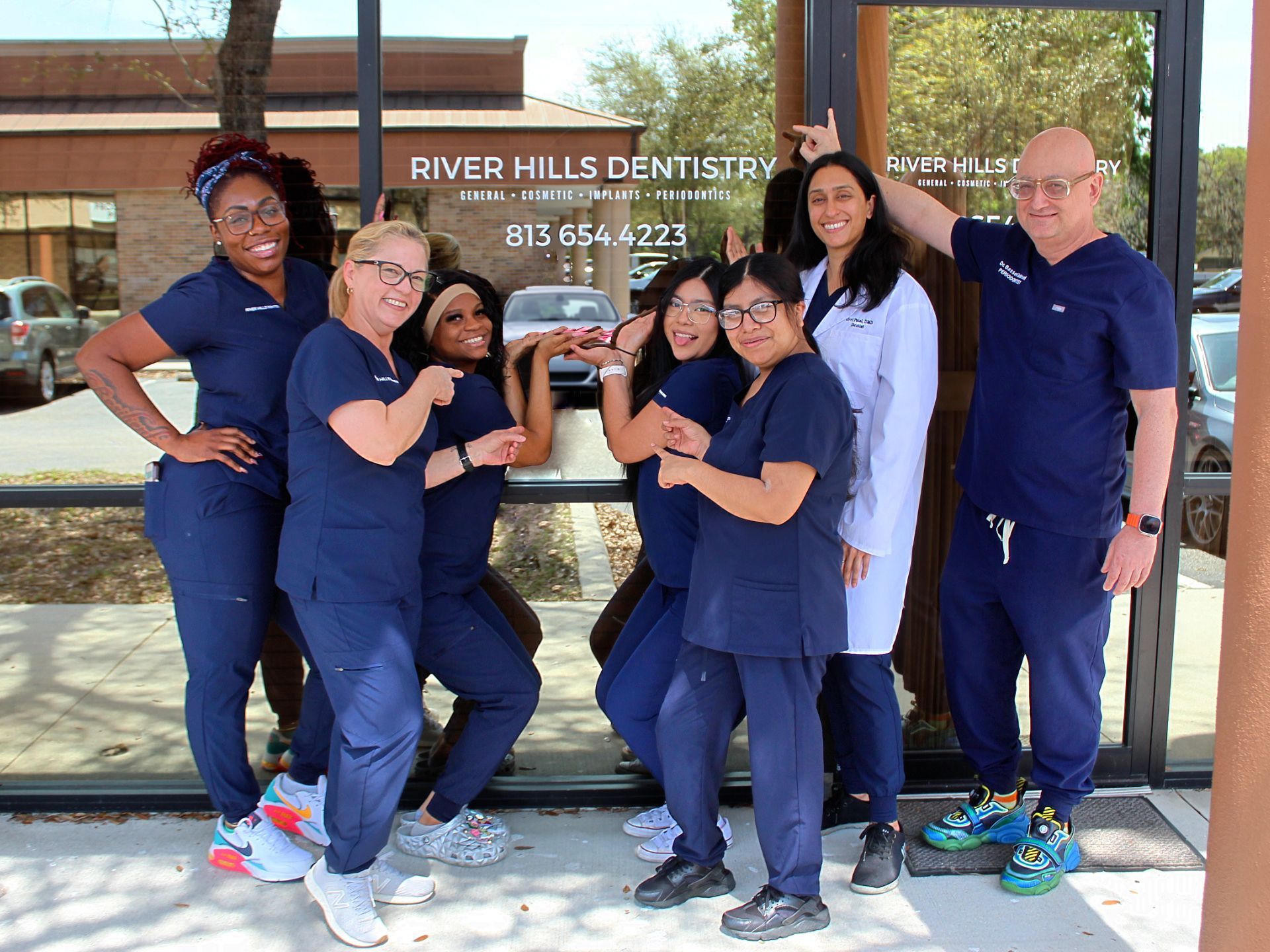 Six dental staff posing outside River Hills Dentistry, smiling in navy scrubs.