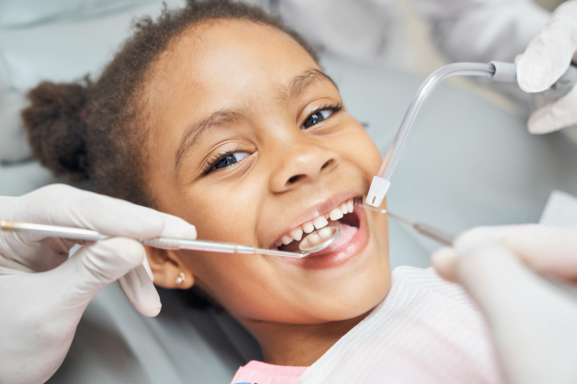 A person receiving a dental checkup with tools in their mouth, smiling while lying in a dentist’s chair.