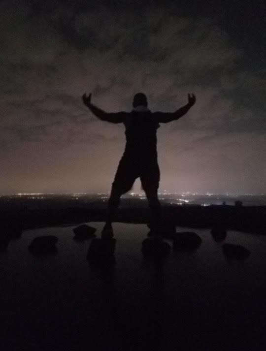 A man is standing in the dark with his arms outstretched.