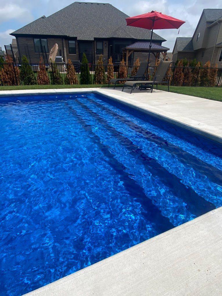 A large swimming pool with a red umbrella in front of a house.