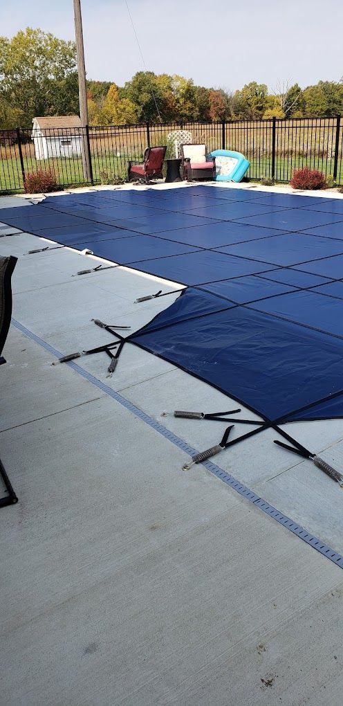 A blue pool cover is sitting on top of a concrete patio next to a swimming pool.