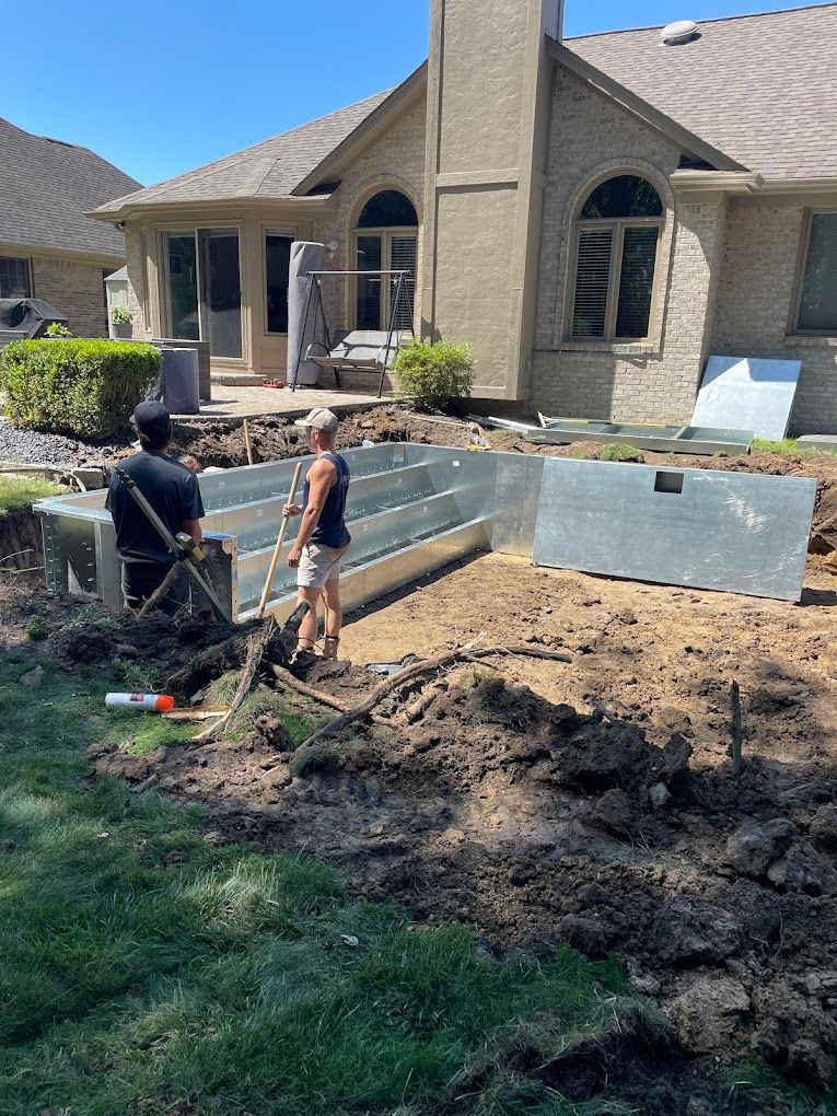 Two men are digging in the dirt in front of a house.