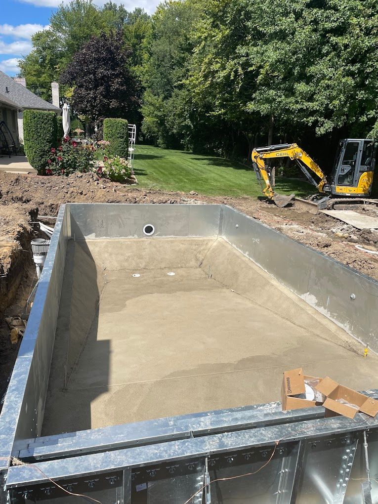 A swimming pool is being built in a backyard with a yellow excavator in the background.