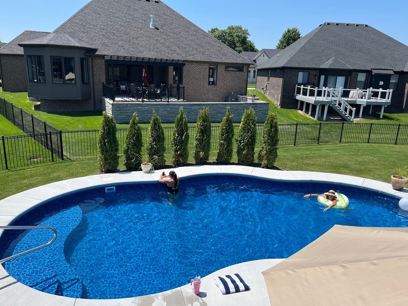 Two people are swimming in a large swimming pool in front of a house.