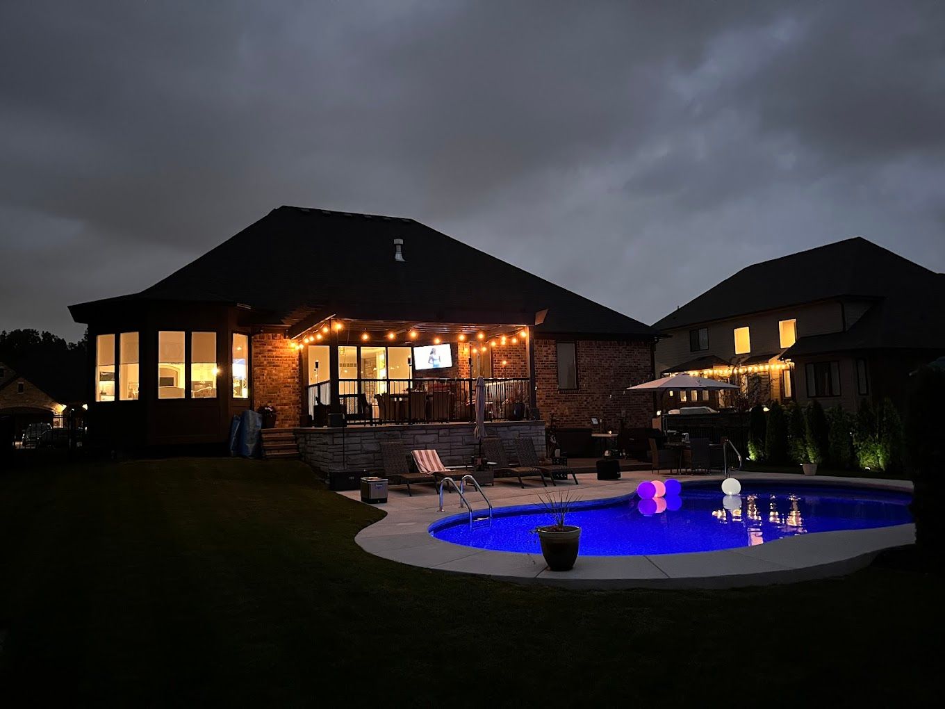 A house with a swimming pool in front of it at night.