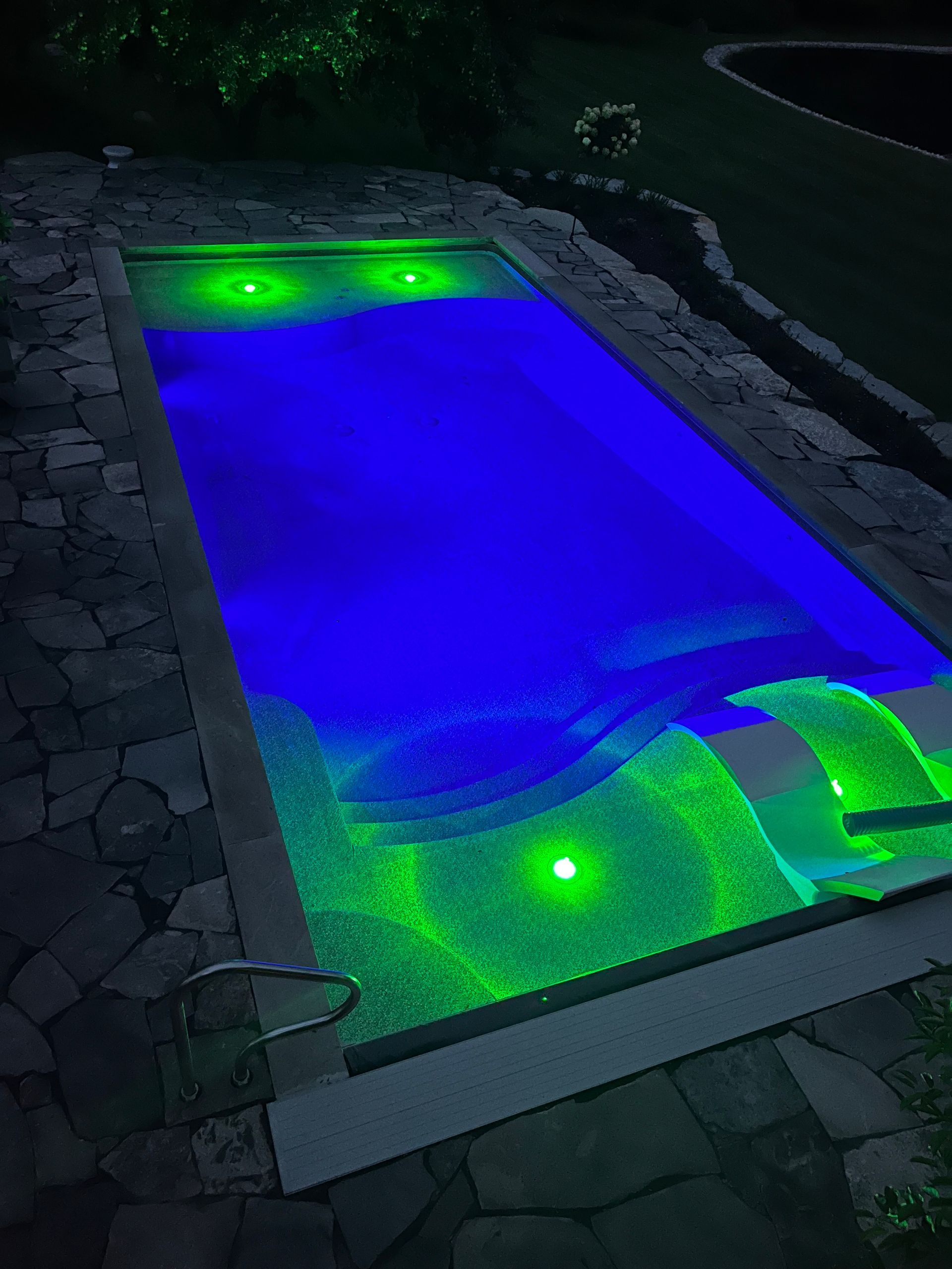 A swimming pool is lit up at night with blue and green lights.