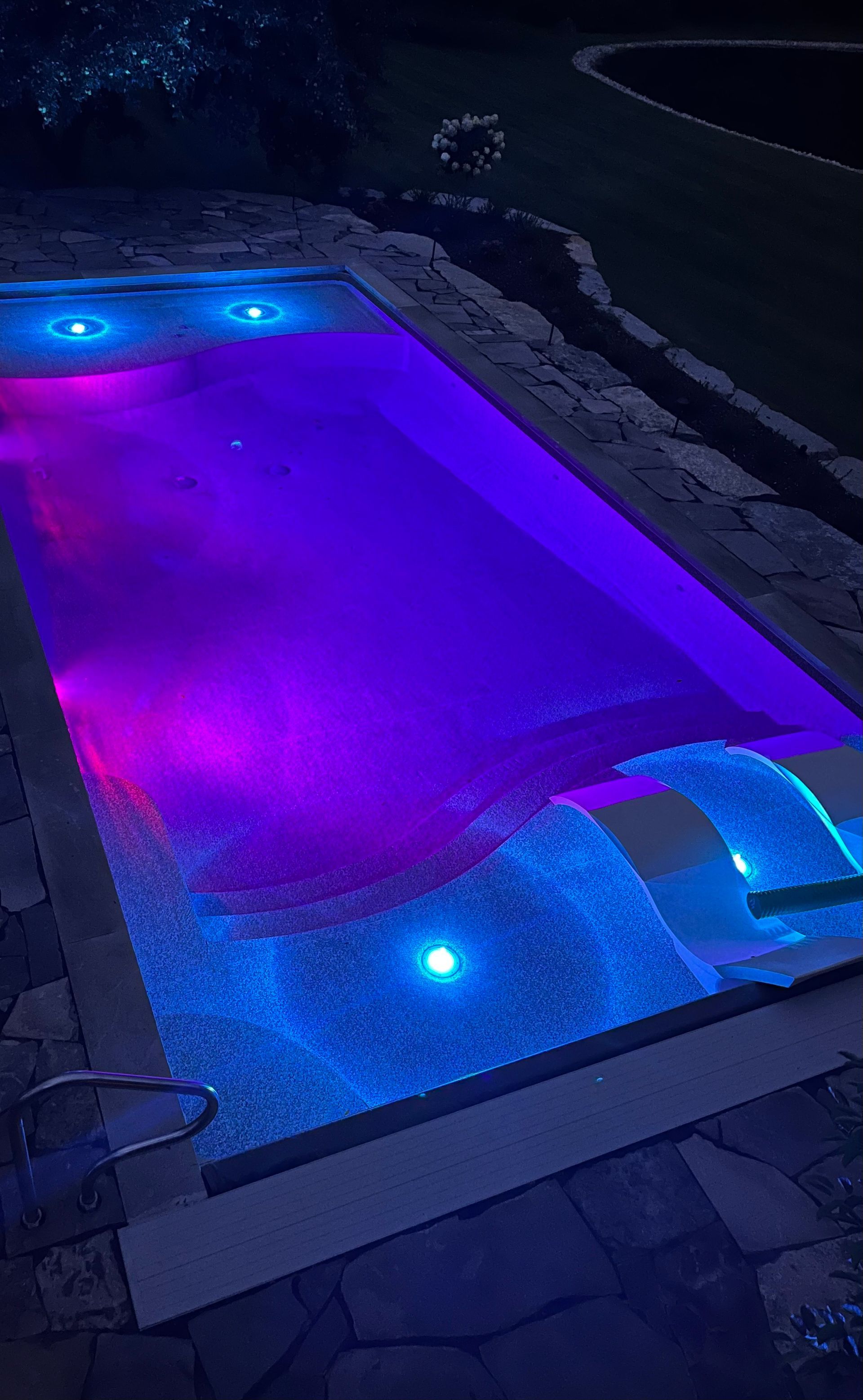 A swimming pool is lit up with purple and blue lights at night.