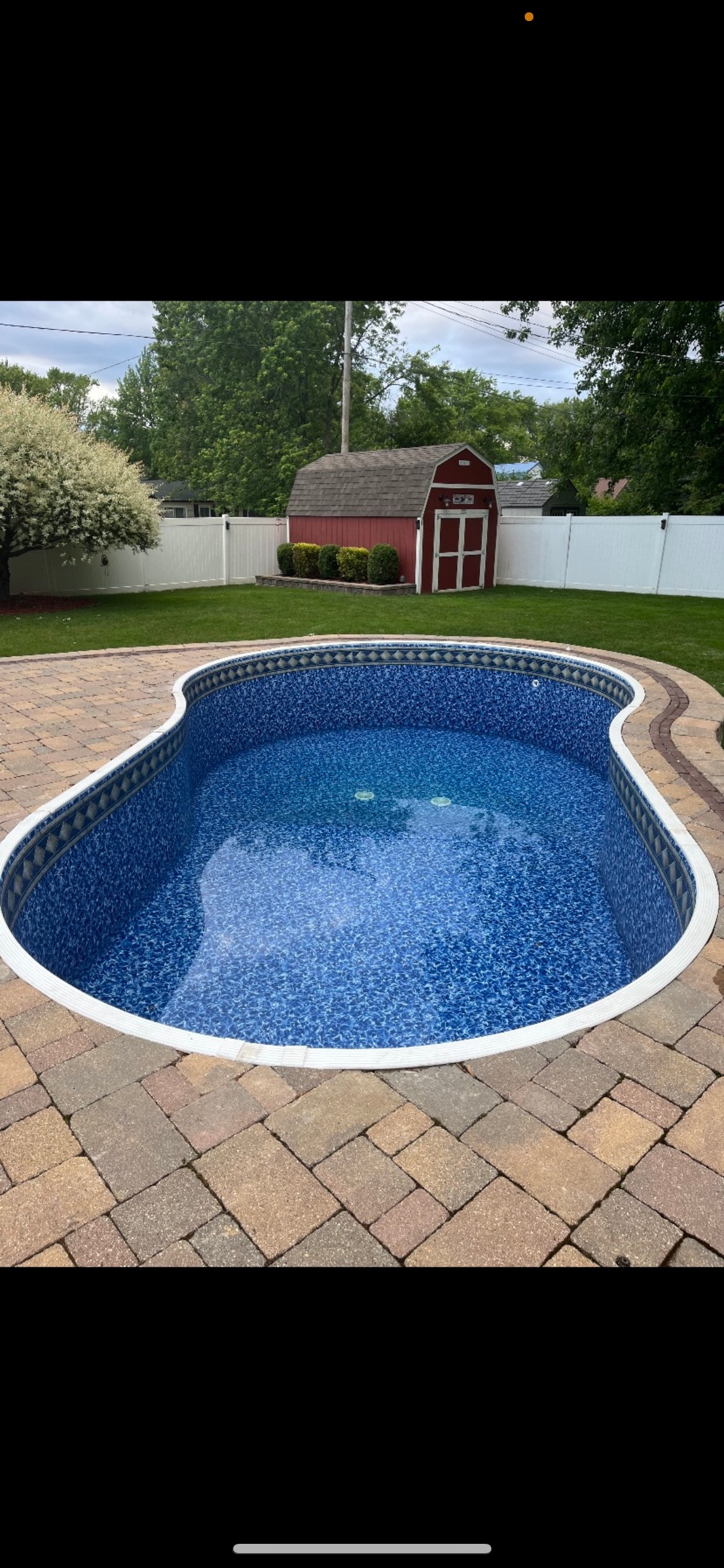A large swimming pool sitting on top of a brick patio next to a barn.