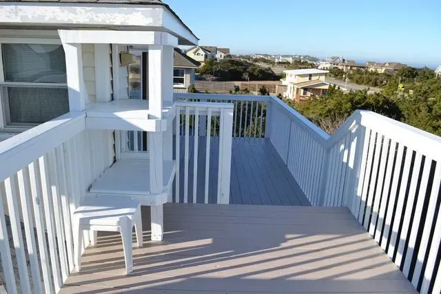 A wooden deck with white railings, a small table, and a built-in shelf structure overlooking a coastal neighborhood.