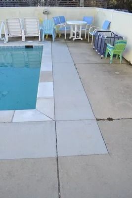 A poolside patio area with white lounge chairs, a small table with chairs, and colorful plastic chairs.