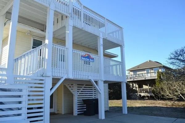 A yellow multi-story beach house with white wooden balconies and stairs, set against a clear blue sky.