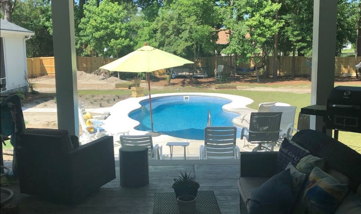 A view from a covered patio overlooking a backyard with a pool, lounge chairs, and a yellow umbrella.