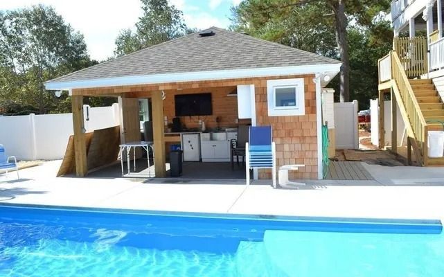 An outdoor kitchen and covered patio area next to a blue swimming pool on a sunny day.