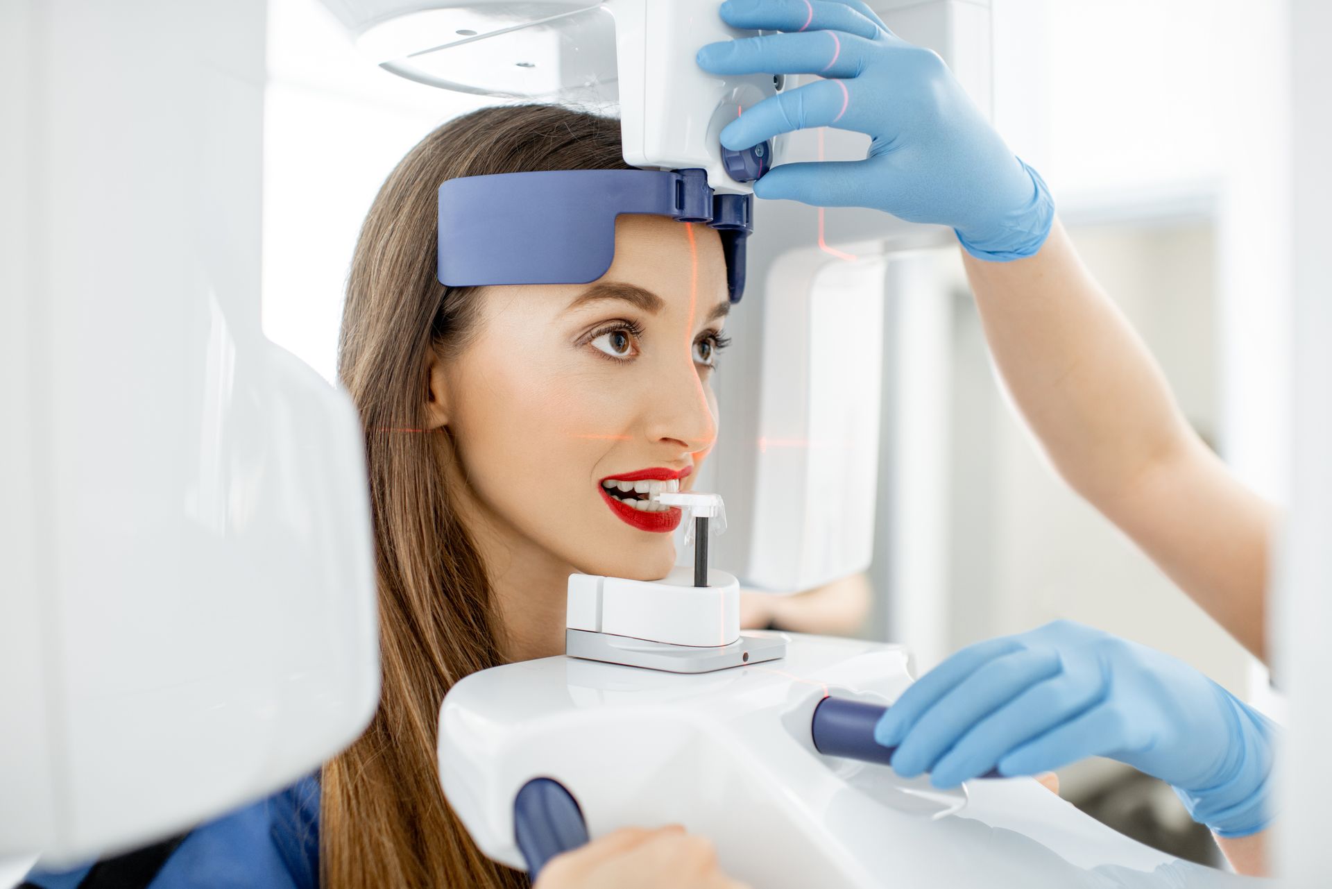 A young woman is getting a panoramic shot of her jaw, holding her face at the X-ray machine.