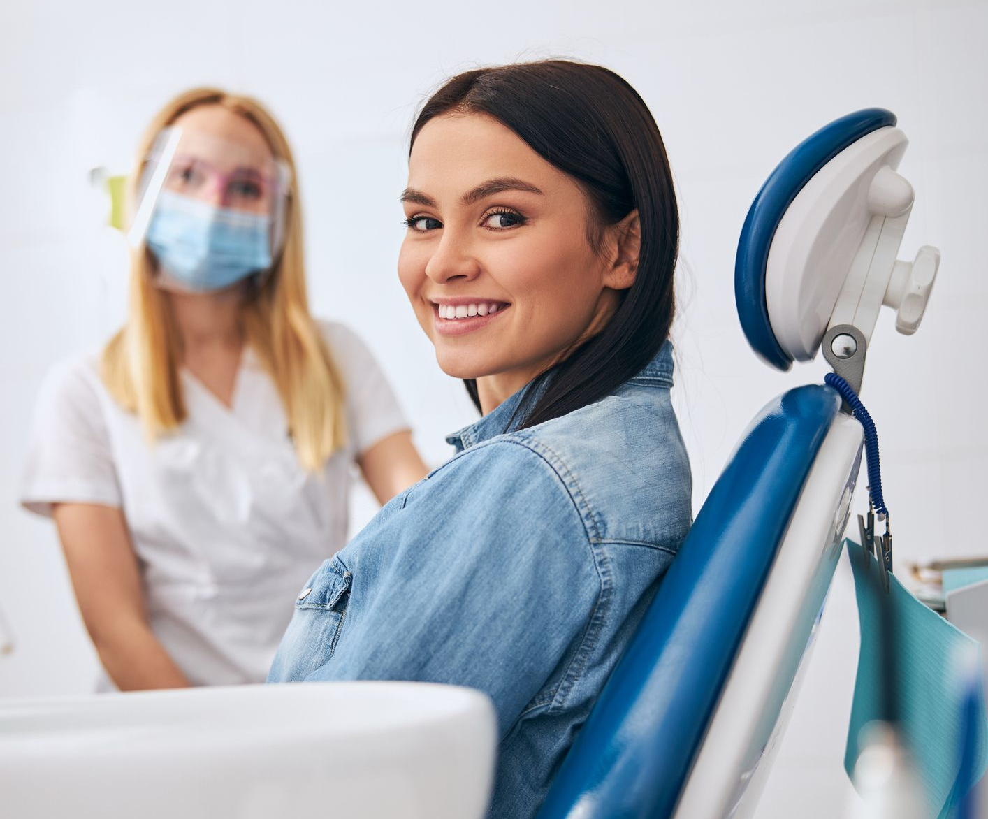 Smiling patient sitting in dental chair at modern dental centre with dentist in background. Smiling patient sitting in dental chair at modern dental centre with dentist in background.