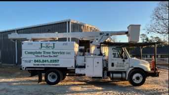 White J&J tree service truck with boom lift parked beside a metal building