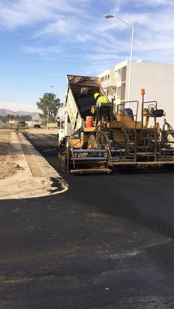 Un hombre está parado encima de una topadora que extiende asfalto en una carretera.