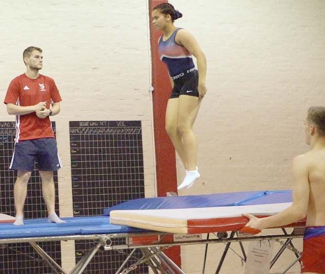 A woman is jumping on a trampoline while two men watch