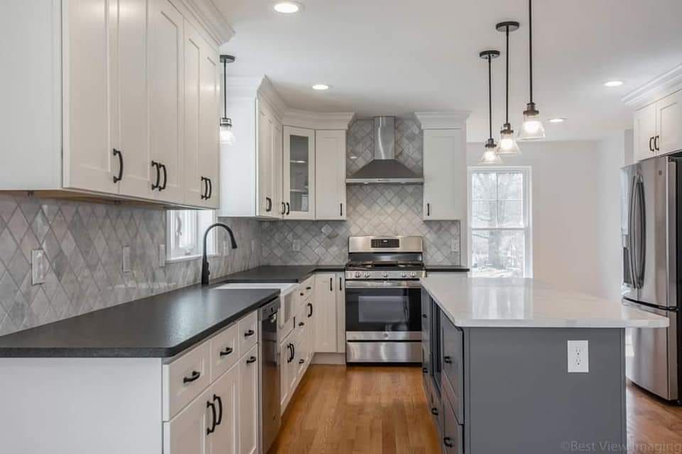 A kitchen with white cabinets , black counter tops , stainless steel appliances and a large island.