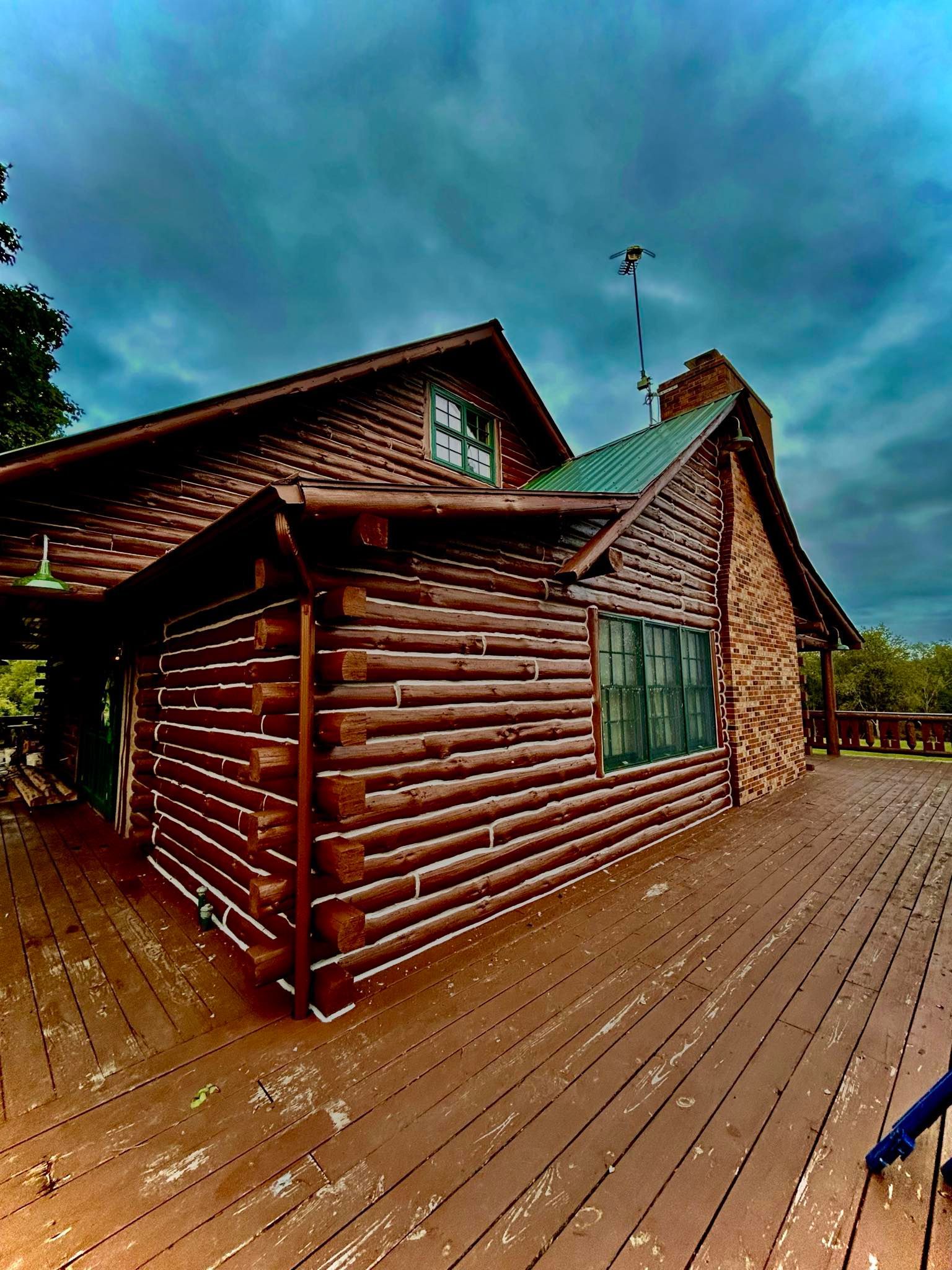 A log cabin with a green roof and a wooden deck