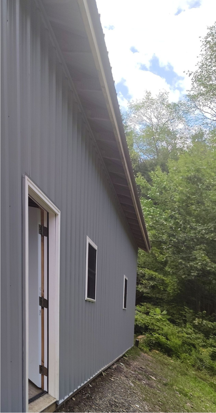 A gray building with a door and windows is sitting in the middle of a forest.