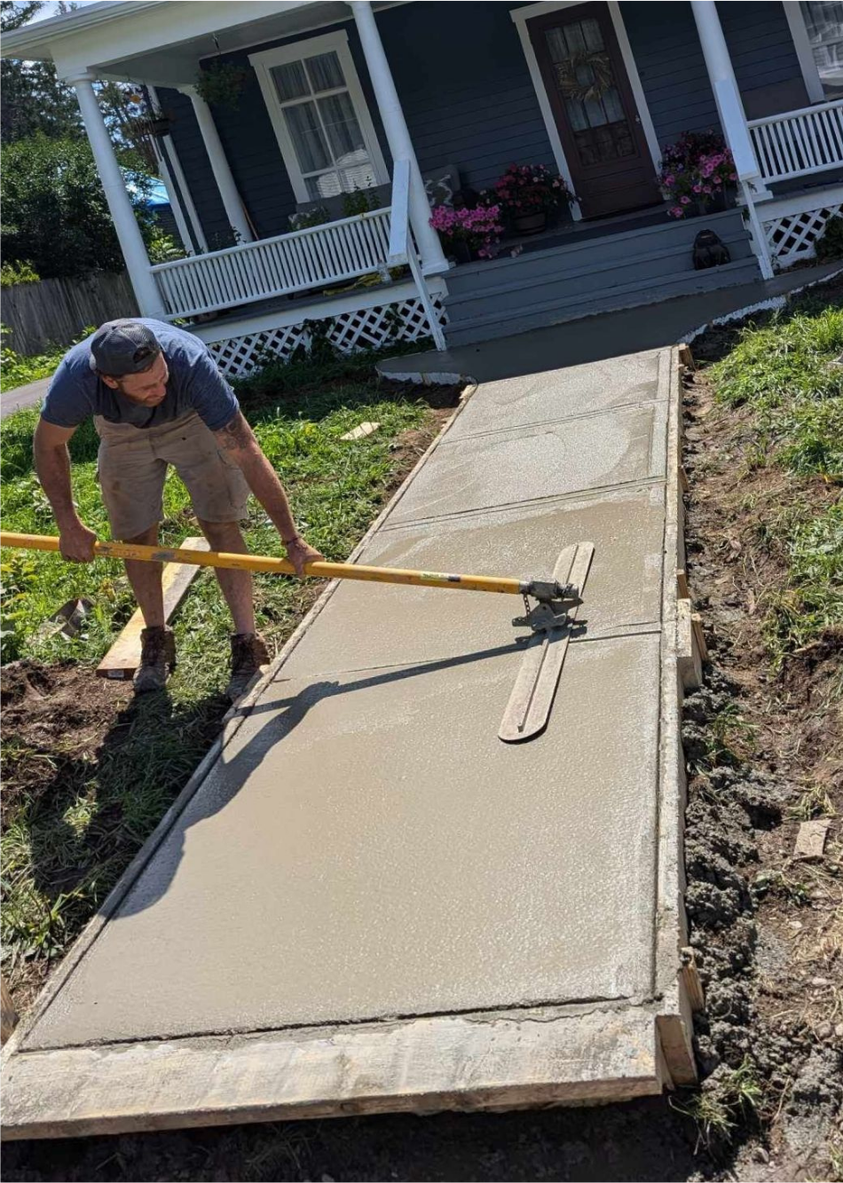 A man is laying concrete on a sidewalk in front of a house.