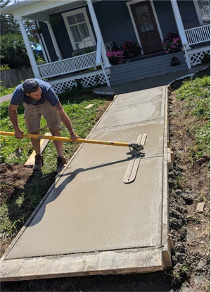 A man is spreading concrete on a sidewalk in front of a house.