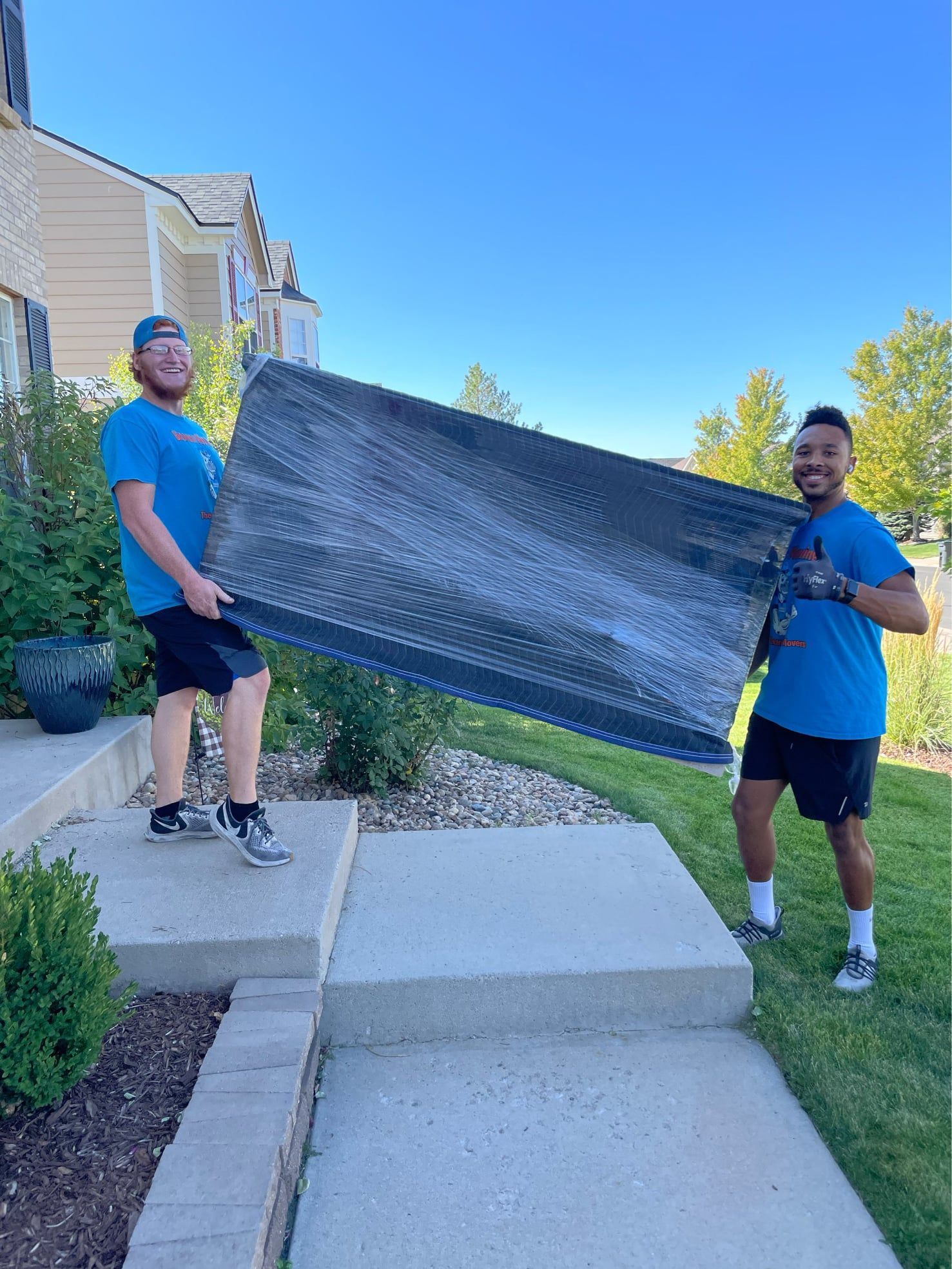 Two movers carrying furniture outside a house.