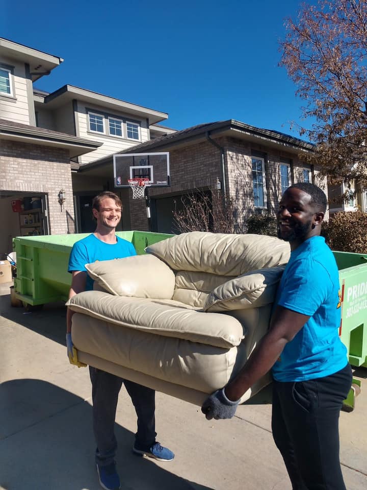 Two movers carrying furniture outside a house.