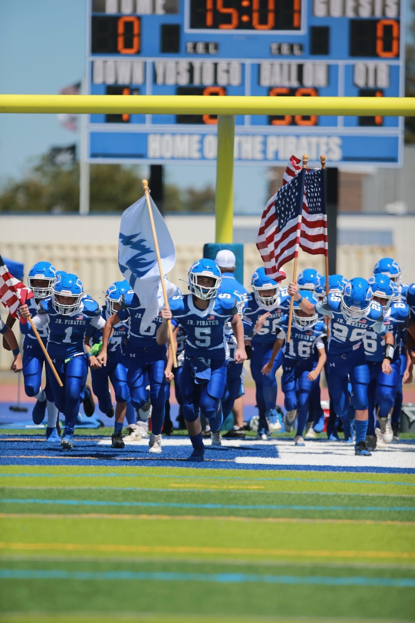 Football player in maroon jersey holding ball, smiling, surrounded by teammates on a field.
