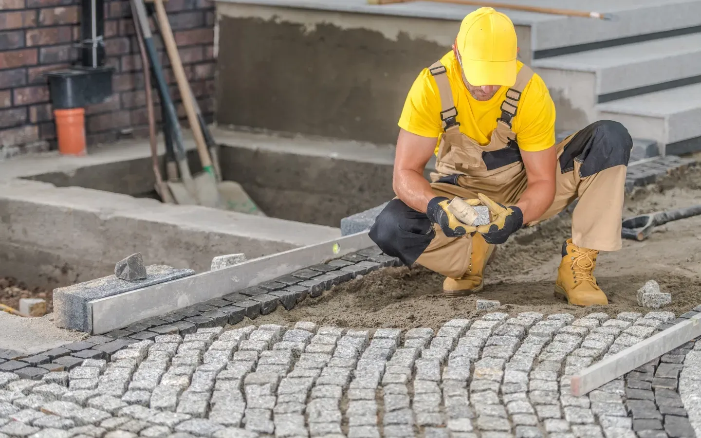 Israel Inc. - A construction worker is kneeling down on a cobblestone sidewalk.