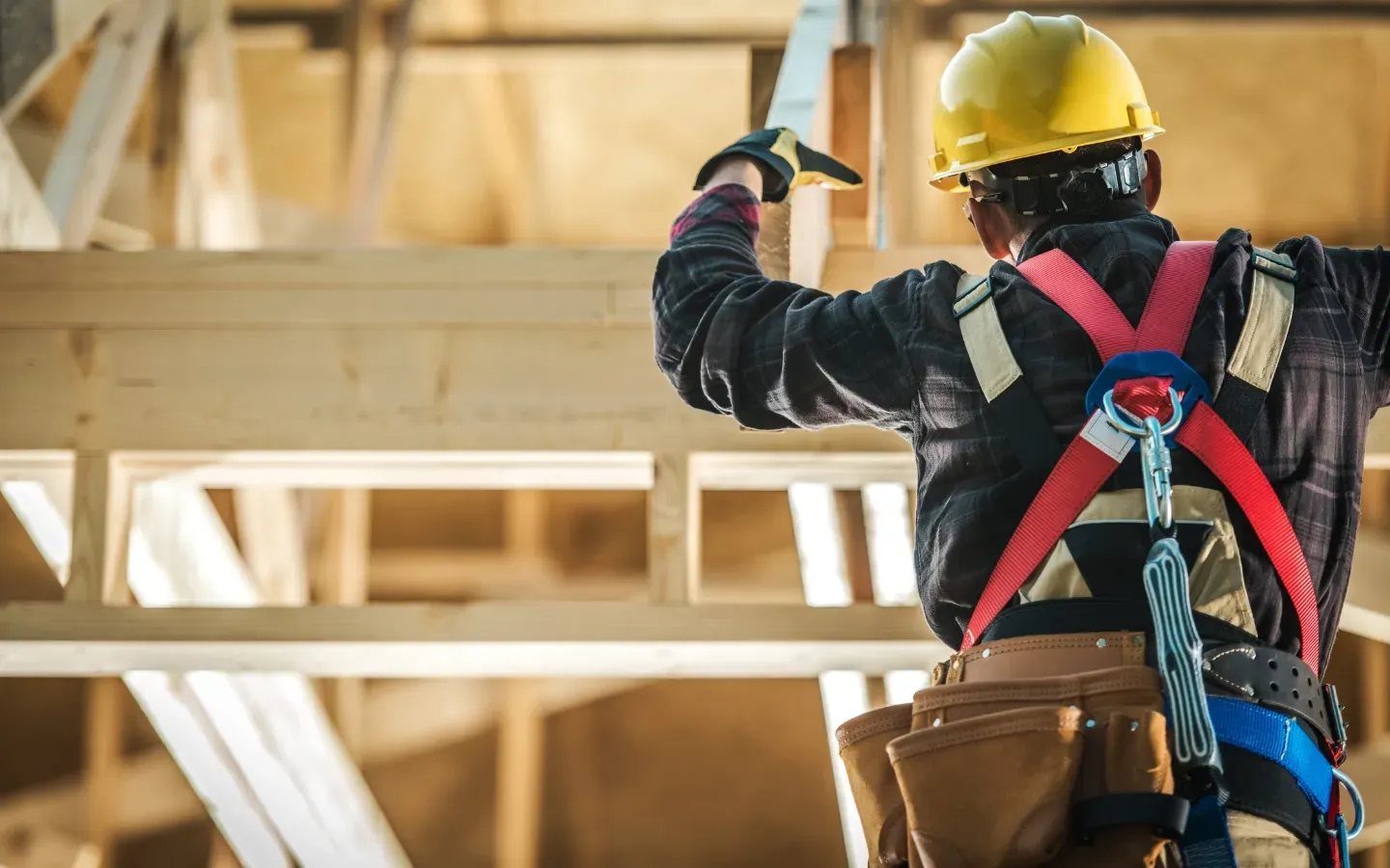 Isreal Inc - A construction worker wearing a hard hat and safety harness is working on a wooden structure.